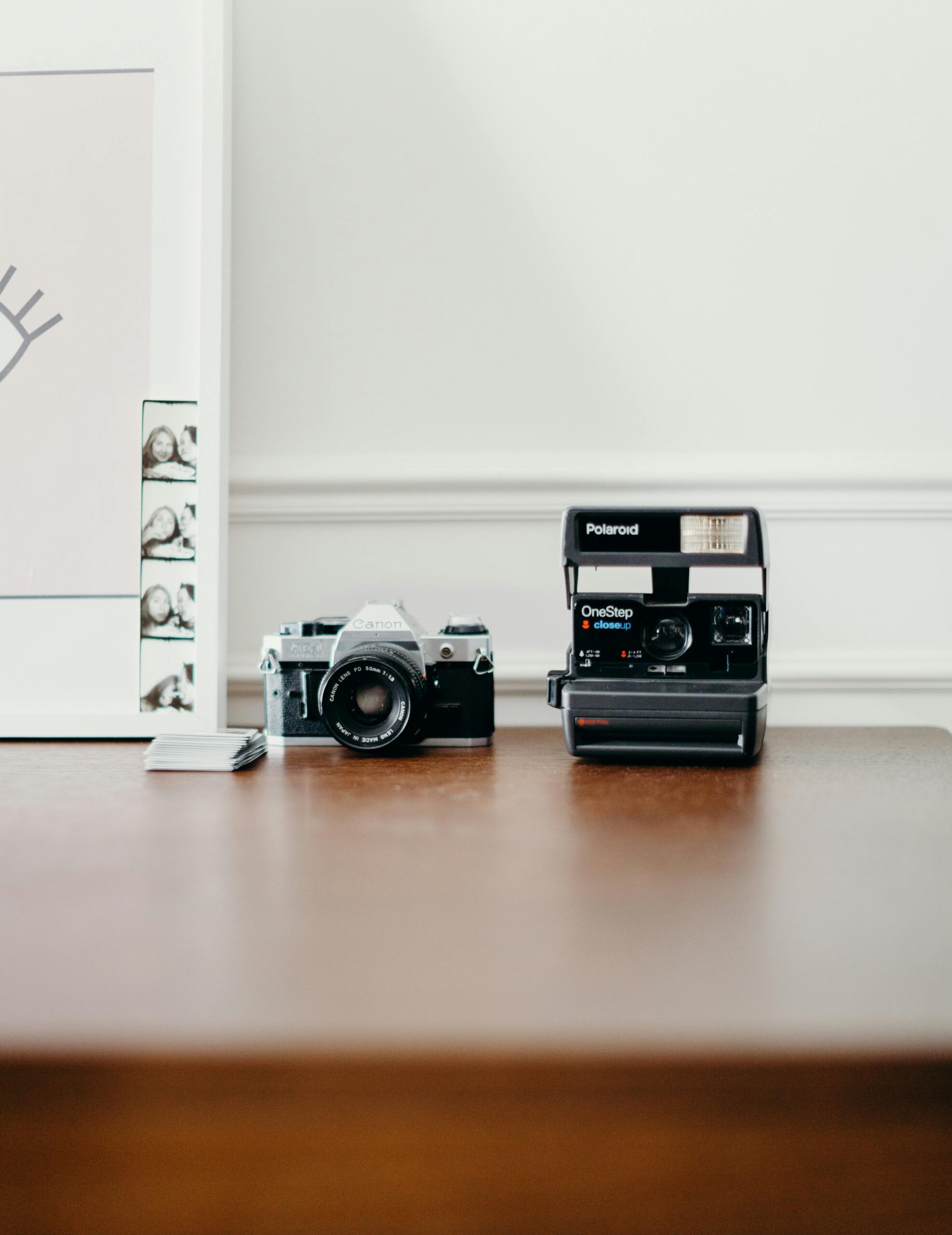 A classic Polaroid OneStep and vintage film camera on a wooden table with a photo frame.