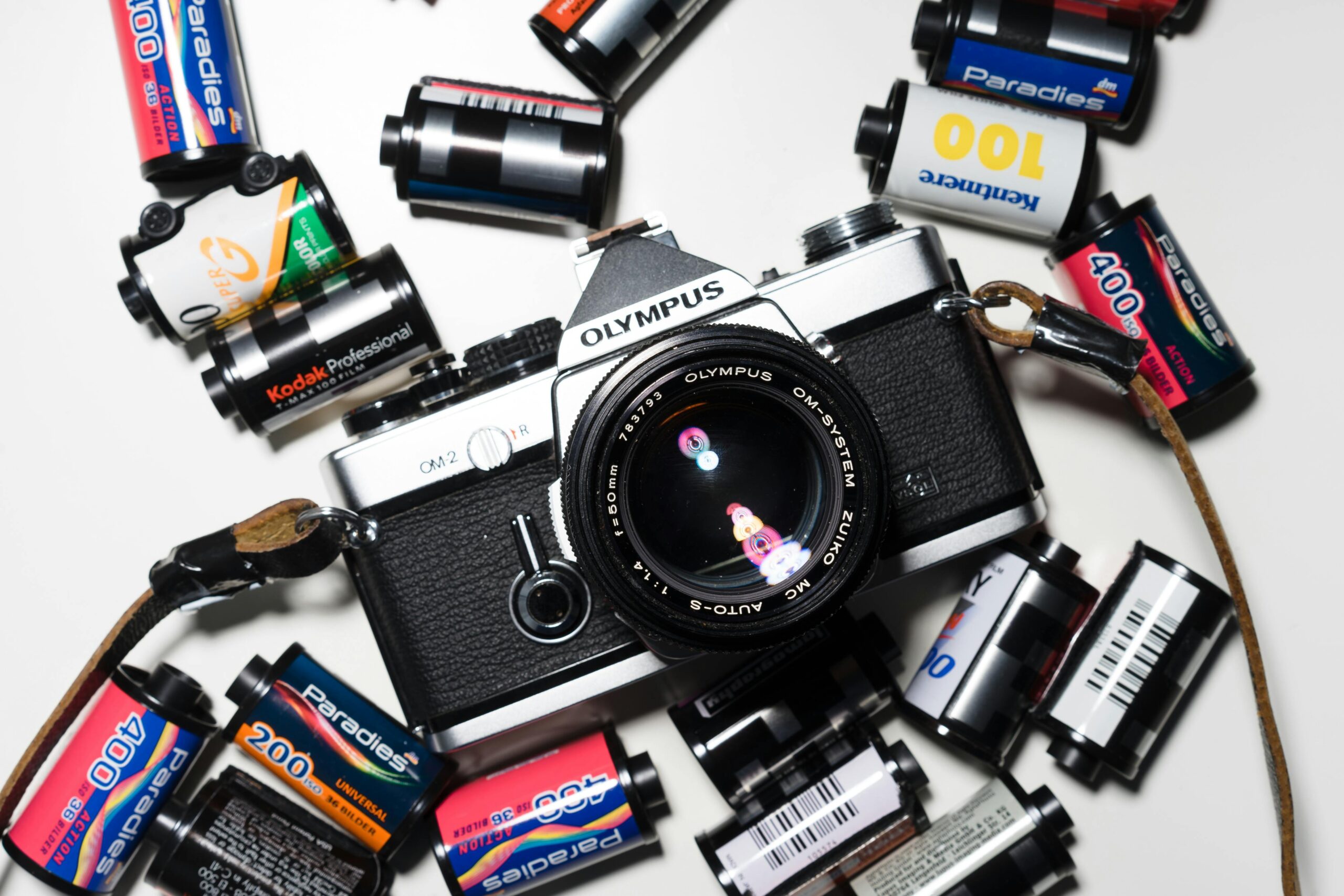 A classic Olympus film camera surrounded by various film rolls on a white surface.